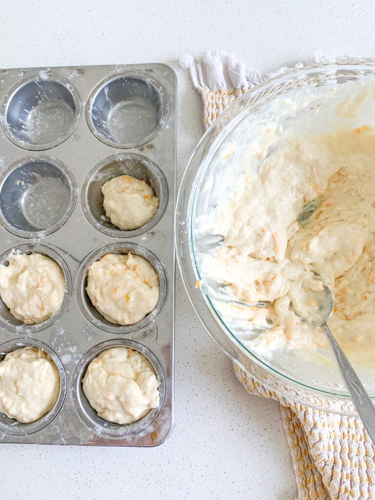 filling muffin tin with cheddar cheese muffin batter