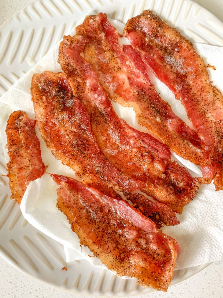 cooked bacon draining on a plate with paper towel