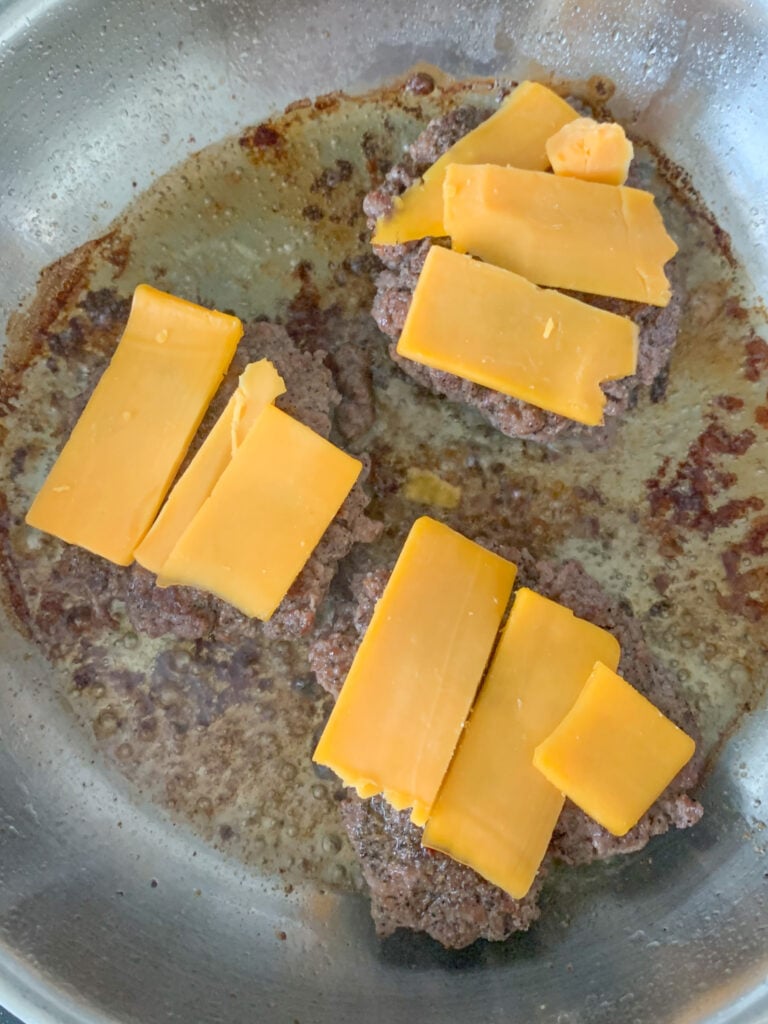 burger patties flipped in the skillet and cheese added on top