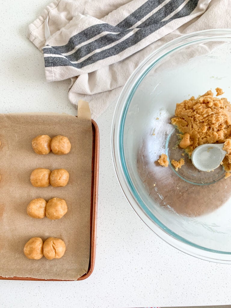 rolling sourdough peanut butter cookie dough into balls on a sheet pan
