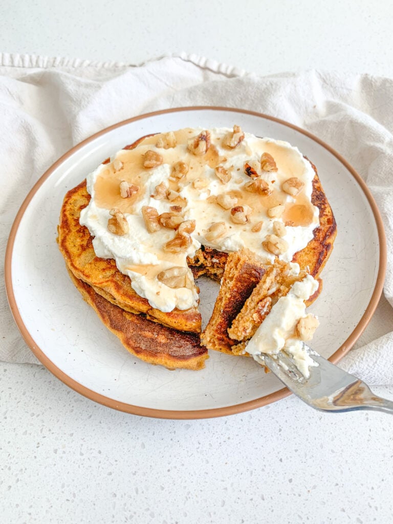 a stack of sourdough pumpkin pancakes freshly made and topped with whipped cream, nuts, and syrup