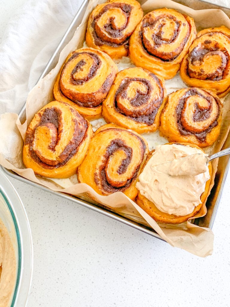 Frosting pumpkin cinnamon rolls after baking