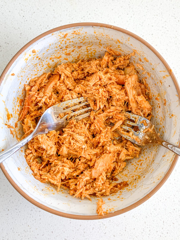 shredding buffalo chicken in a bowl after cooking